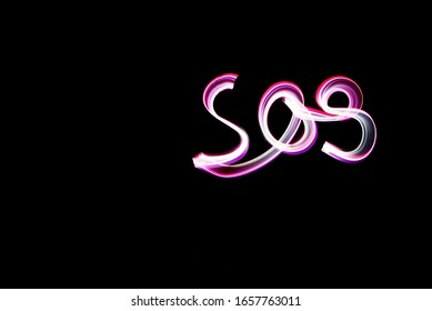 Handwritten Word SOS, Light Painting Experiment With Bulb Exposure, At Night. Black Background With Copy Space Left