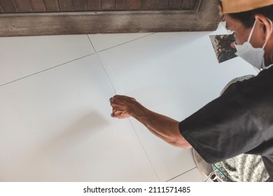 A handy man applies grout to fill the gaps of white porcelain floor tiles at the living room. Home renovation or finishing works.
