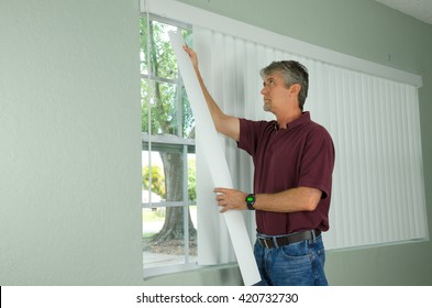 A handy man home repair service technician or home owner hanging white vertical blinds for the window treatment in a new house.