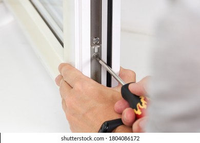 Handyman Adjusting White Pvc Plastic Window Indoors. Worker Using Screwdriver To Repair Upvc Window. Homework Maintenance.