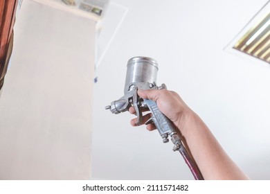 A Handyman Applies A First Coat Of Wood Primer On The End Panel Of A Cabinet. Using An Airbrush For The Application. Home Renovation Or Finishing Works.