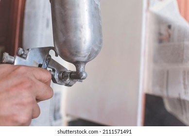 A Handyman Applies A First Coat Of Wood Primer On The End Panel Of A Cabinet. Using An Airbrush For The Application. Home Renovation Or Finishing Works.