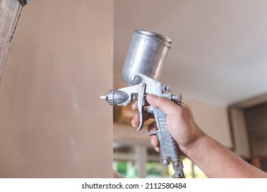 A Handyman Applies A First Coat Of Wood Primer On The End Panel Of A Cabinet. Using An Airbrush For The Application. Home Renovation Or Finishing Works.