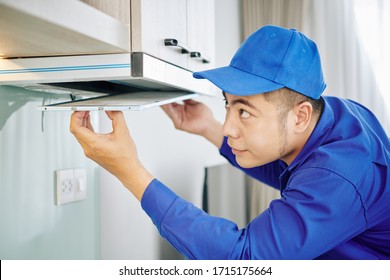 Handyman in blue uniform installing or repairing cooker hood in kitchen of customer