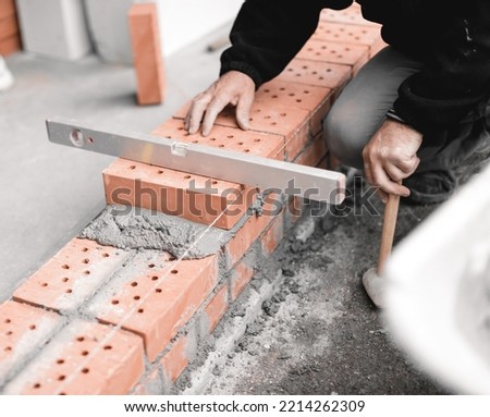 handyman checking the surface level of the brick wall with the spirit level