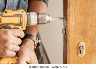 Handyman, drill door and wood for handle at workplace, industry and home development goals. Hands, tools and construction worker with maintenance, property management and diy carpenter for building