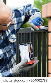 Handyman Holding A Can Of Paint And Painting Metal Fence