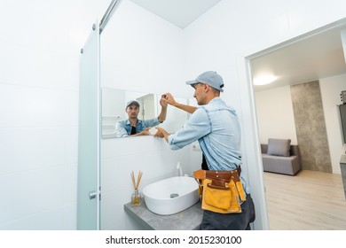 Handyman installing mirror in bathroom.
