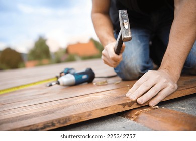 Handyman installing wooden flooring in patio, working with hammer - Powered by Shutterstock