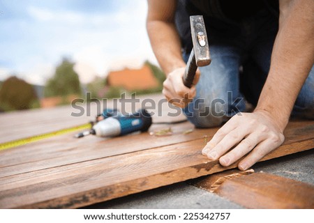 Handyman installing wooden flooring in patio, working with hammer