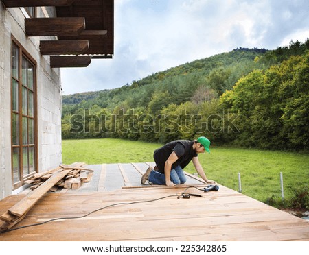 Handyman installing wooden flooring in patio, working with drilling machine