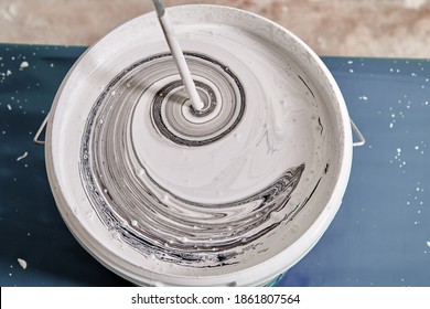 Handyman is mixing black and white colors using painting mixer in the basket to get a gray color. Worker mixes paints with help of drill.
