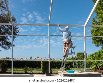 Handyman On Ladder Cleaning Outdoor Pool Cage Enclosure. Screened Swimming Pool Lanai Maintenance And Screen Repair.