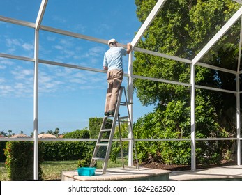 Handyman on ladder cleaning outdoor pool cage enclosure. Screened swimming pool lanai maintenance and screen repair.