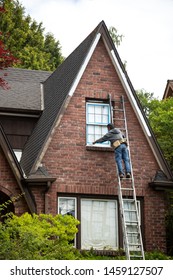 Handyman On A Ladder Painting The Windowsill Of An Old Brick House, In A Home Remodel Scene With Space For Text On Top And Bottom