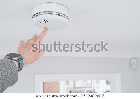 Handyman seen doing a weekly test of a combine smoke and carbon monoxide tester in a home hallway. The detector is wired into the house wiring a requires no battery.