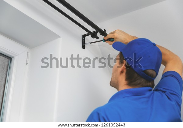 handyman services - worker installing window curtain\
rod on the wall