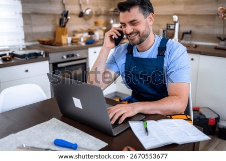 Handyman sits at a table in a kitchen, making phone calls and managing repair tasks online.