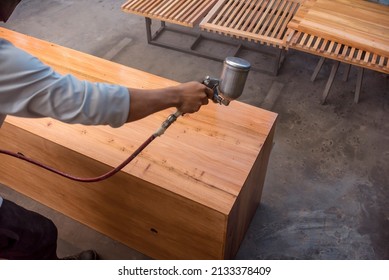 A Handyman Sprays Lacquer Wood Finish On A Shelf Or Cabinet. Using An Airbrush For The Application. At A Furniture And Woodworking Shop.