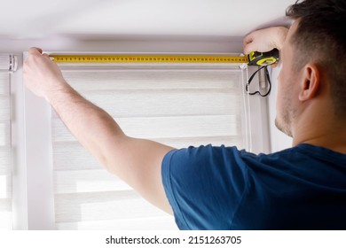 A handyman with a tape measure installs white roller blinds indoors. Shutters day and night. - Shutterstock ID 2151263705