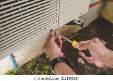 A Handyman Unscrews The Front Hatch Of The Outside Compressor Unit Of Split Type Air Conditioner Unit. Repair Or Maintenance Work.