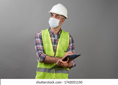 Handyman Worker Checking The List On The Clipboard. Worker Man Wearing Face Mask With Protective Hard Hat And Safety Vest