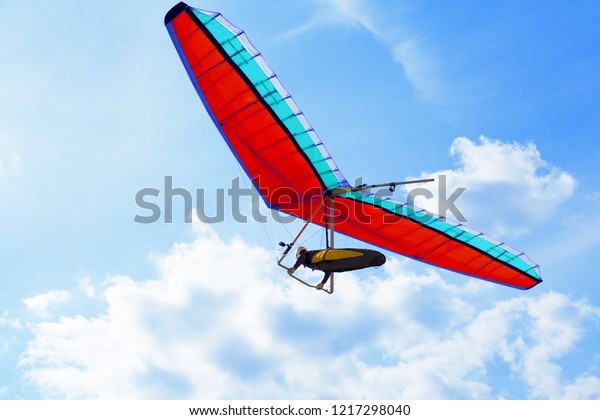 The hang glider on a red hang-glider is flying in a\
blue sky