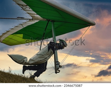 Hang glider pilot runs from the hill into sunset sky.