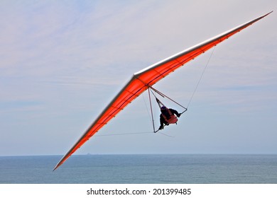 Hang Gliding Man On An Orange Wing With Sky In The Background