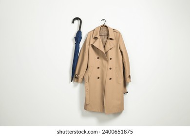 Hanger with beige trench coat and blue umbrella on white wall, space for text - Powered by Shutterstock