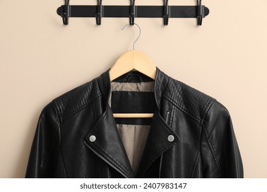 Hanger with black leather jacket on beige wall