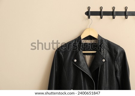 Hanger with black leather jacket on beige wall, space for text
