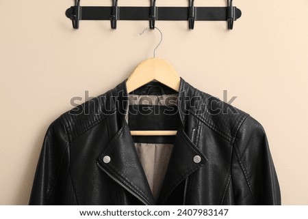 Hanger with black leather jacket on beige wall