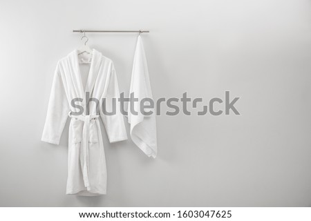 Hanger with clean bathrobe and towel on light wall. Space for text
