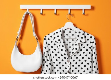 Hanger with polka dot shirt and bag on orange wall - Powered by Shutterstock