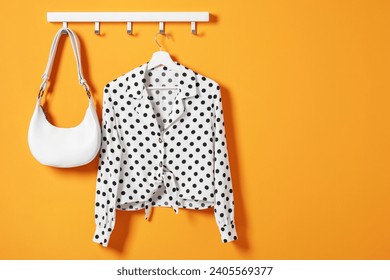 Hanger with polka dot shirt and bag on orange wall, space for text - Powered by Shutterstock