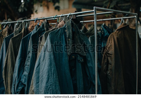 Hanger stand with vintage wax jackets.\
Secondhand brown jackets ,sweater and different Winter jackets.\
Men\'s wax jackets on hangers\
outdoors.