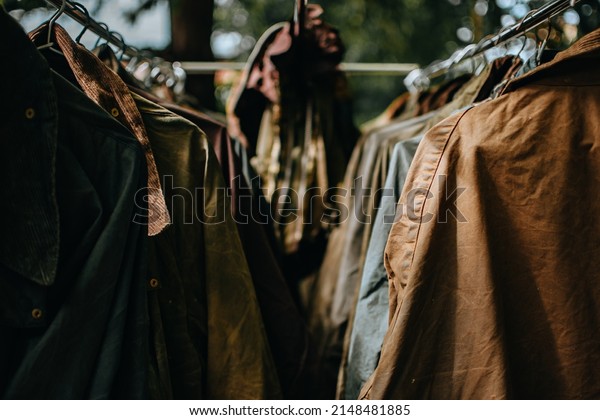 Hanger stand with vintage wax jackets.\
Secondhand brown jackets ,sweater and different Winter jackets.\
Men\'s wax jackets on hangers\
outdoors.