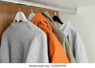 Hangers With Different Clothes In Open Wooden Wardrobe Closet. Selection Of A Wardrobe, Stylist, Shopping.