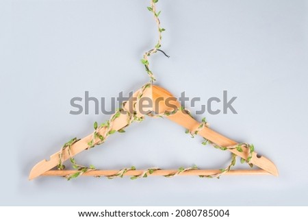 Hangers entwined with plants on gray background with copyspace. Conscious and environmentally friendly consupmtion - new modern trends in shopping. Zero waste. Slow fashion concept.