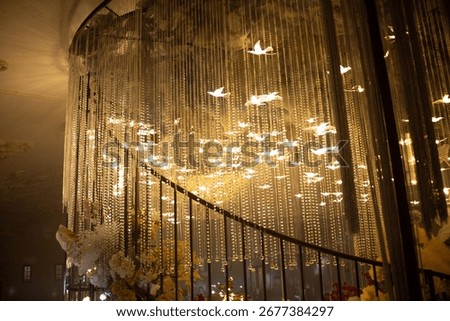Hanging cascade of glowing with golden tiny birds floating strands of light sparkling like stars in midair luminous waterfall chandelier