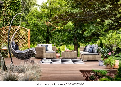 Hanging Chair And Geometric Carpet On Wooden Patio With Rattan Garden Furniture