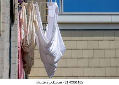 Hanging Clothes On The Clothesline Outside The Building In The City, Drying Laundry Under The Sun In Summer, White Sheet On The Washing Line On The High Floor, Fabric And Linen Background.