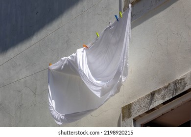 Hanging Clothes On The Clothesline Outside Building, Typical Portuguese Style Drying Laundry Under The Sun In Summer, White Sheet On The Washing Line In City With Cement Wall As Background, Portugal