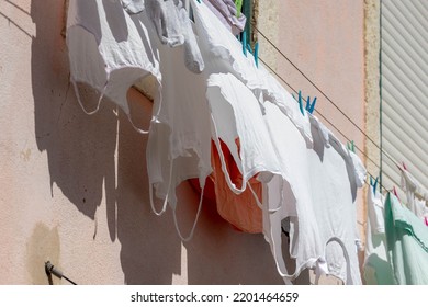 Hanging Clothes On The Clothesline Outside Building, Typical Portuguese Style Drying Laundry Under The Sun In Summer, White T-shirt On The Washing Line In City With Cement Wall As Background, Portugal