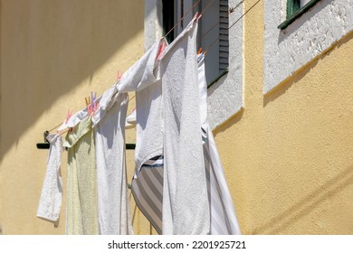 Hanging Clothes On The Clothesline Outside Building, Typical Portuguese Style Drying Laundry Under The Sun In Summer, White Towels On The Washing Line In City With Cement Wall As Background, Portugal.