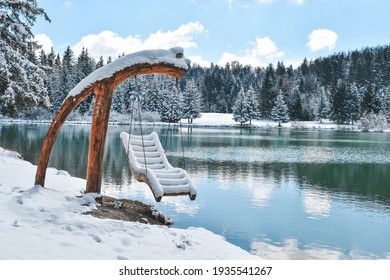 Hanging deck chair covered with snow on the shore of Lake Bloke. An untouched scene with a forest reflecting on a surface of the water - Shutterstock ID 1935541267