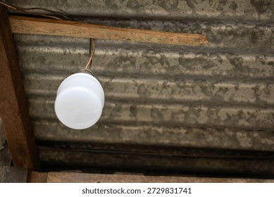 Hanging LED light bulb on corrugated metal ceiling, indoor photo in natural light