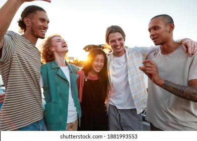 Hanging out. A group of young well-dressed friends of different nationalities hugging each other having a good time together outside laughing and smiling during a beautiful sunset