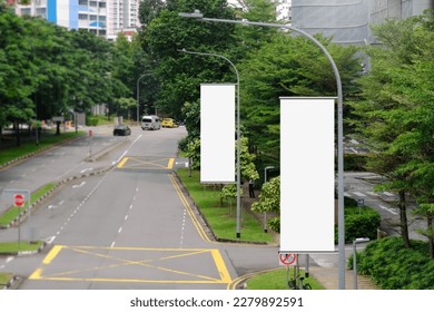 Hanging posters by the road in the city; blank vertical advertising banners on street lampposts, against lush green trees and plants. For OOH out of home template mock up. - Shutterstock ID 2279892591